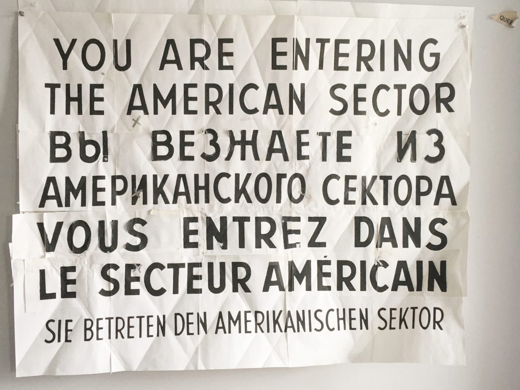 Image:'Checkpoint Charlie' sign on paper. It reads, 'You Are Now Entering the American Sector' in English, Russian, French and German.